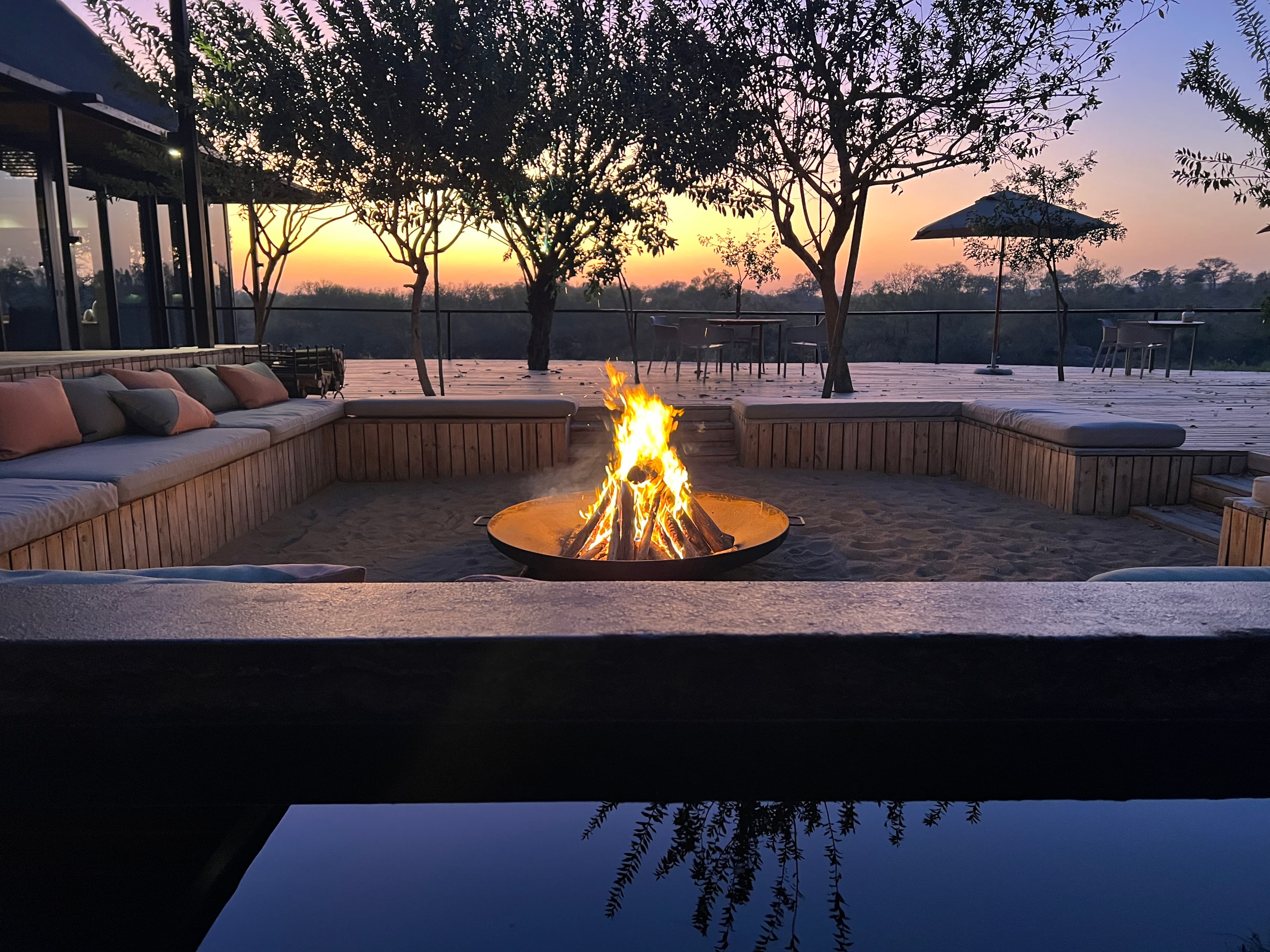 Fire pit blazing at sunset on a premium safari lodge deck with pool reflection