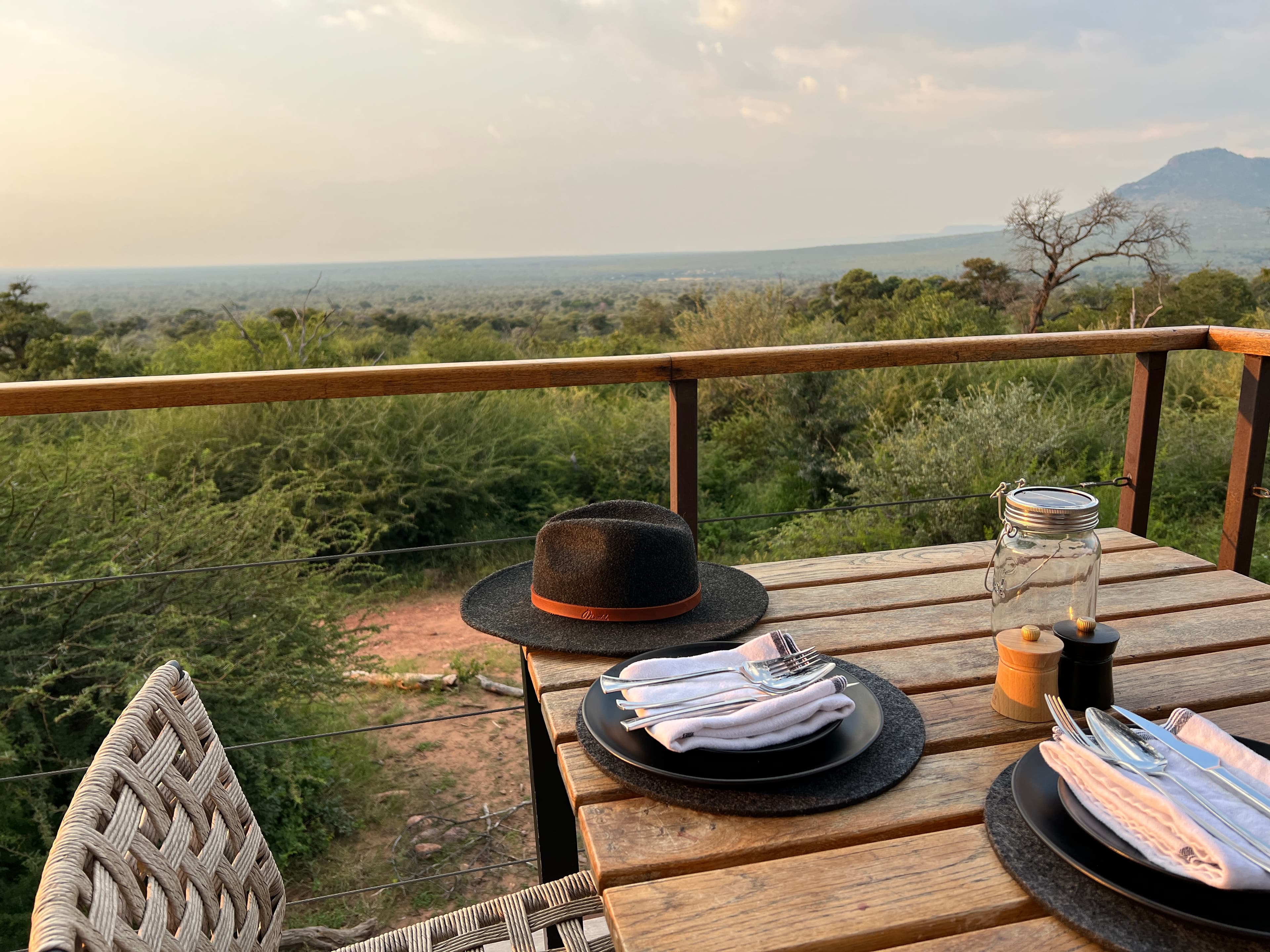 Lodge dining deck with safari hat overlooking the African bush at dusk